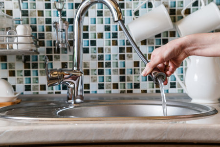 A housewife girl uses a kitchen faucet with a hose for washing dishes.の写真素材
