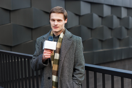 A young stylishly dressed male TV reporter is reporting on the street in the city.の写真素材