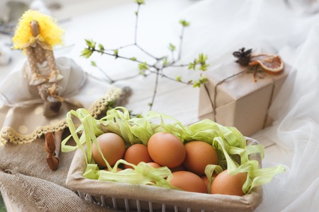 Spring composition. A toy doll, eggs in a basket and a festive box with a gift.の写真素材