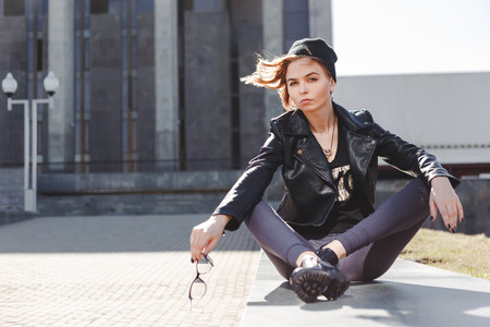 Portrait of fashionable impudent blonde girl with eye glasses wearing a rock black style outdoors in the city.の写真素材