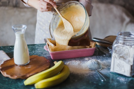 Woman baker is pouring dough into a baking tray. Cooking the banana pieの写真素材