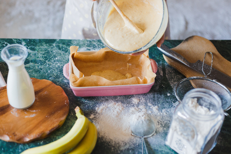 Woman baker is pouring dough into a baking tray. Cooking the banana pie.の写真素材