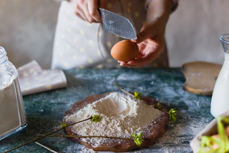 Breaking an egg with a knife into a hill of flour. Cooking baking. Female hand baker close-up. Before the cracking.の写真素材