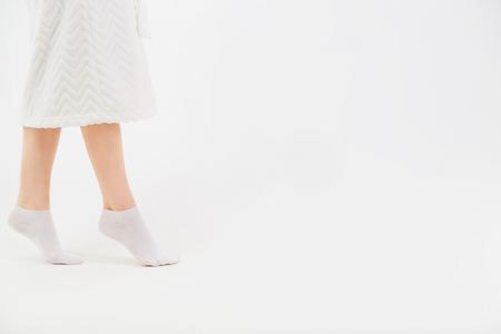 A girl in a white bathrobe and socks goes on socks after a shower. Close-up of beautiful female slender legs. Side view. Barefoot helth conceptの写真素材