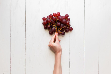 The girl's hand holds on to a bunch of red grapes on a wooden background. View from above. Grapes are like balloonsの写真素材