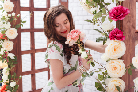 Beautiful young brunette woman with long curly hair is smelling the flowersの写真素材