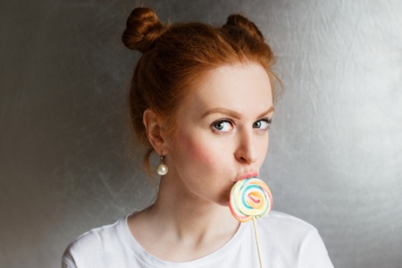 Redhead beautiful girl with multi-colored round candy and funny hairstyle on silver background.の写真素材