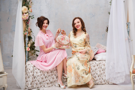 Happy girlfriends smile and show each other jewelry, sitting in their bedroom.の写真素材