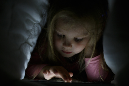 Little girl is playing on the tablet in secret from her parents at night under the blanket.の写真素材