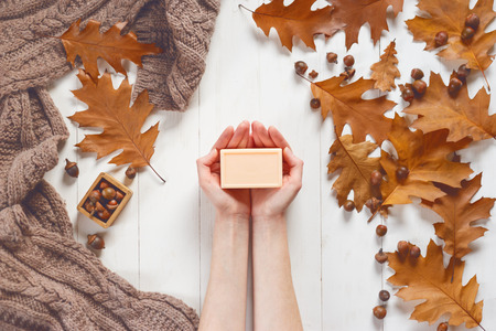 Piece of soap flesh-colored in female hands in a composition with a soft scarf and oak leaves. View from above. The concept of beauty and care for body and hands.の写真素材