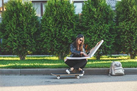 Young fashionably dressed girl sitting with pizza box on loan and has a lunchの写真素材