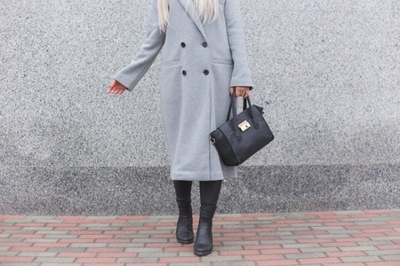 Fashionable woman posing outdoor, holding black leather bag, wearing stylish boots, elegant coat. Female fashion conceptの写真素材