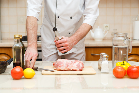 Mans hand holds bottle with souce. Professional cook prepare the meatの写真素材