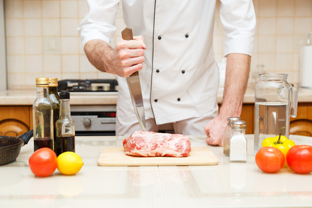 Butcher cutting meat on chopping board, professional cook holding knife and cutting meat.の写真素材