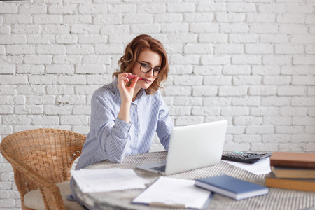 Happy woman sitting at office and holding a pen in her mouthの写真素材