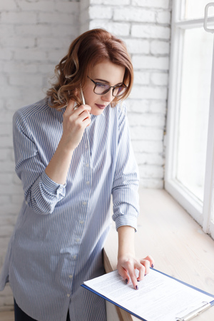 Young businesswoman consulting a document as she talks on the phone in the office, close up profile viewの写真素材