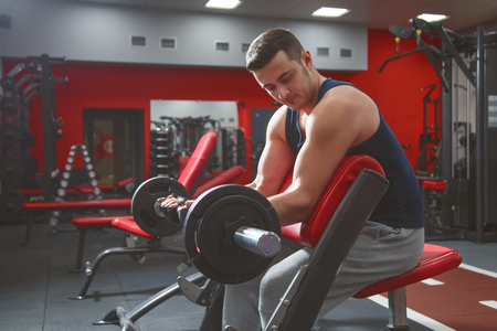 Handsome man doing biceps lifting barbell on bench in a gymの写真素材