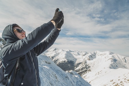 Handsome man in sunglasses take a photo with a smartphone in snowy mountains.の写真素材