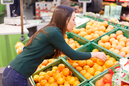 A young woman in a store chooses oranges.の写真素材