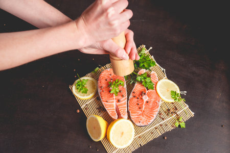 A woman sprinkles salmon with pepper from a pepper mill