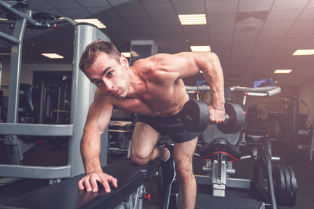 Sportsman doing dumbbell rows on bench at gym.の写真素材