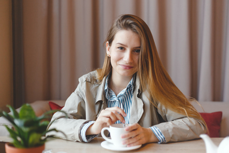 Beautiful young woman with coffee cup looking away at coffeeshopの写真素材
