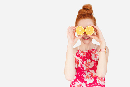 Young ginger hair woman smiling with two halves of lemon on her eyes.の写真素材