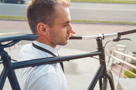Handsome young businessman in a white shirt and black tie carries his bikeの写真素材