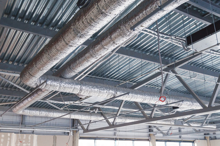 HVAC. Ventilation pipes in silver insulation material hanging from the ceiling inside new building.の写真素材