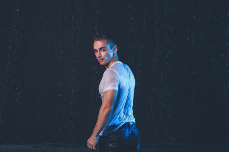 Fresh portrait of muscular man with water splashes on dark background.