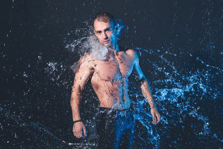 Fresh portrait of muscular man with water splashes on dark background.の写真素材