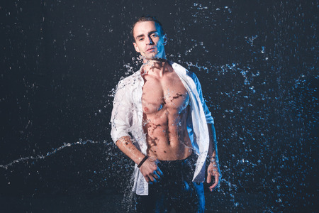 Fresh portrait of muscular man with water splashes on dark background.の写真素材