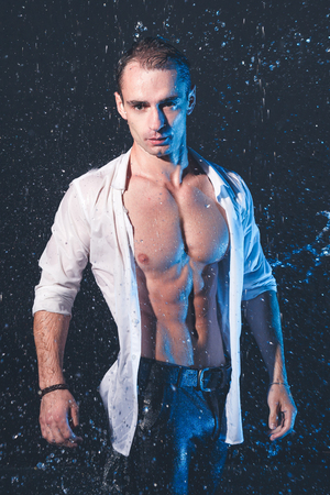 Fresh portrait of muscular man with water splashes on dark background.の写真素材