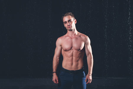 Fresh portrait of muscular man with water splashes on dark background.の写真素材