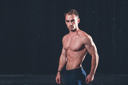 Fresh portrait of muscular man with water splashes on dark background.の写真素材