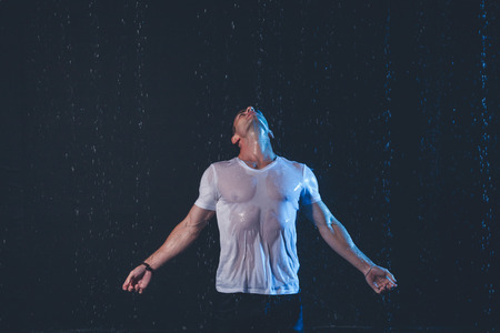 Fresh portrait of muscular man with water splashes on dark background.の写真素材