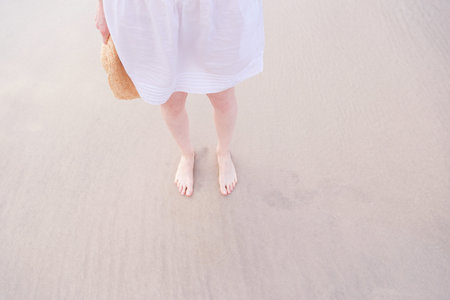 Legs of woman relax in white dress on a beach sea sand.