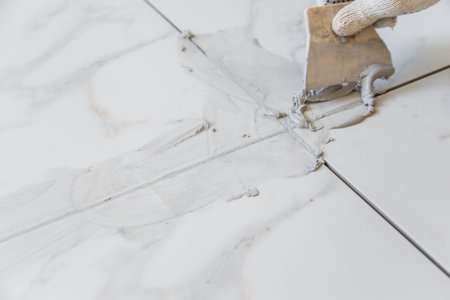 Grouting tiles seams with a rubber trowel.