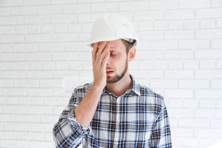 A blue collar worker wearing a hardhat is covering his face with his hand.の写真素材