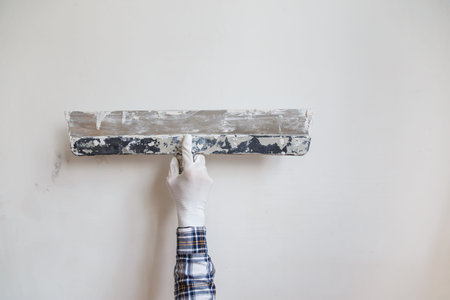 Worker in white gloves performs plastering of the walls of the room