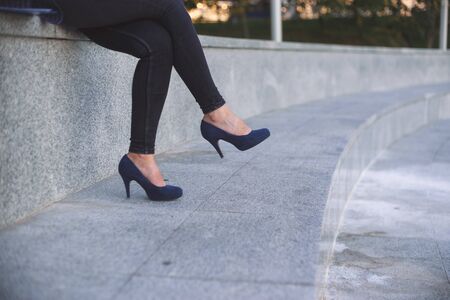 Young office woman blue jeans wearing high-heeled shoes, sitting cross-legged outdoor.の写真素材