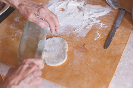 Hands of an old woman on flattened dough.