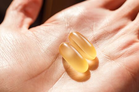 Two softgels of fish oil daily. Capsules on handの写真素材