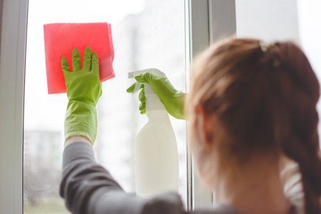Women cleaning a window with spray and cloth. Close up view