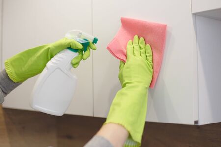Woman is cleaning kitchen cabinet door with rag and spray detergent in kitchenの写真素材