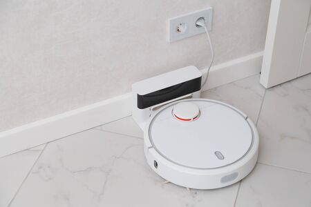 Robot vacuum cleaner on charging. Room with white ceramic tile and walls.の写真素材