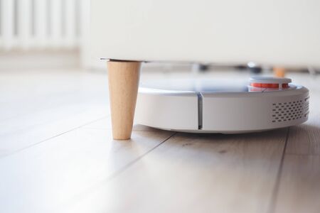 Robot vacuum cleaner is vacuuming under the bed. Cleaning in inaccessible places. Automation and smart home, modern technologyの写真素材