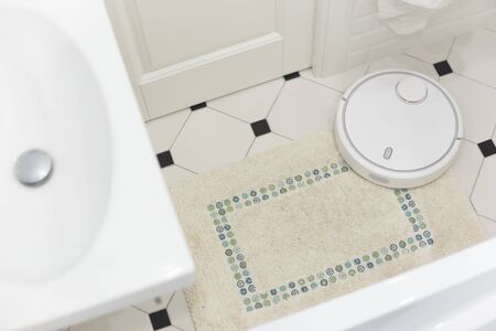 White robot vacuum cleaner on carpet in bathroom.の写真素材