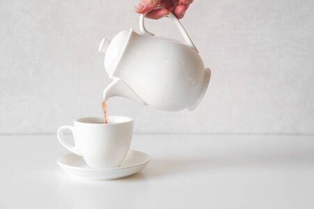 Pouring fresh tea from porcelain tea kettle into white cup.の写真素材