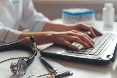 Female doctor diagnostician at his workplace in the hospital. Works on laptop with x-ray and medical testsの写真素材